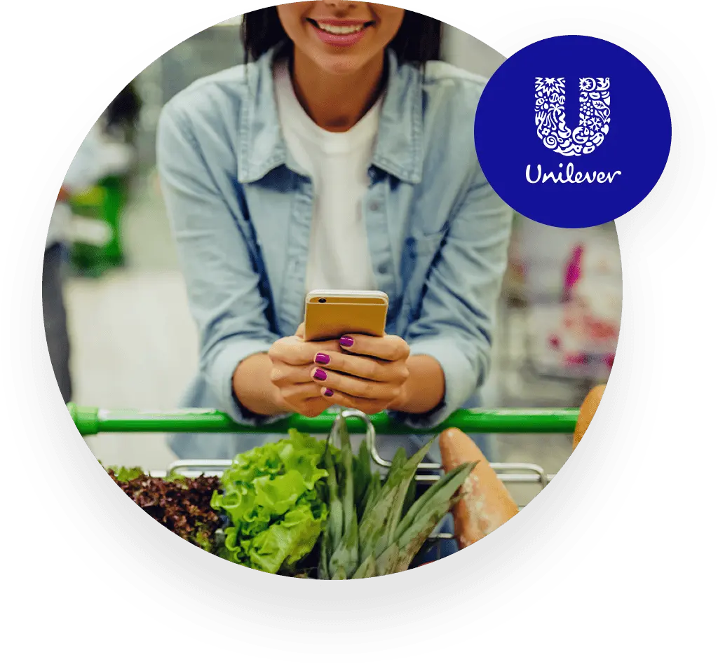 Eine Frau hält ihr Smartphone und lächelt (Unilever-Logo)